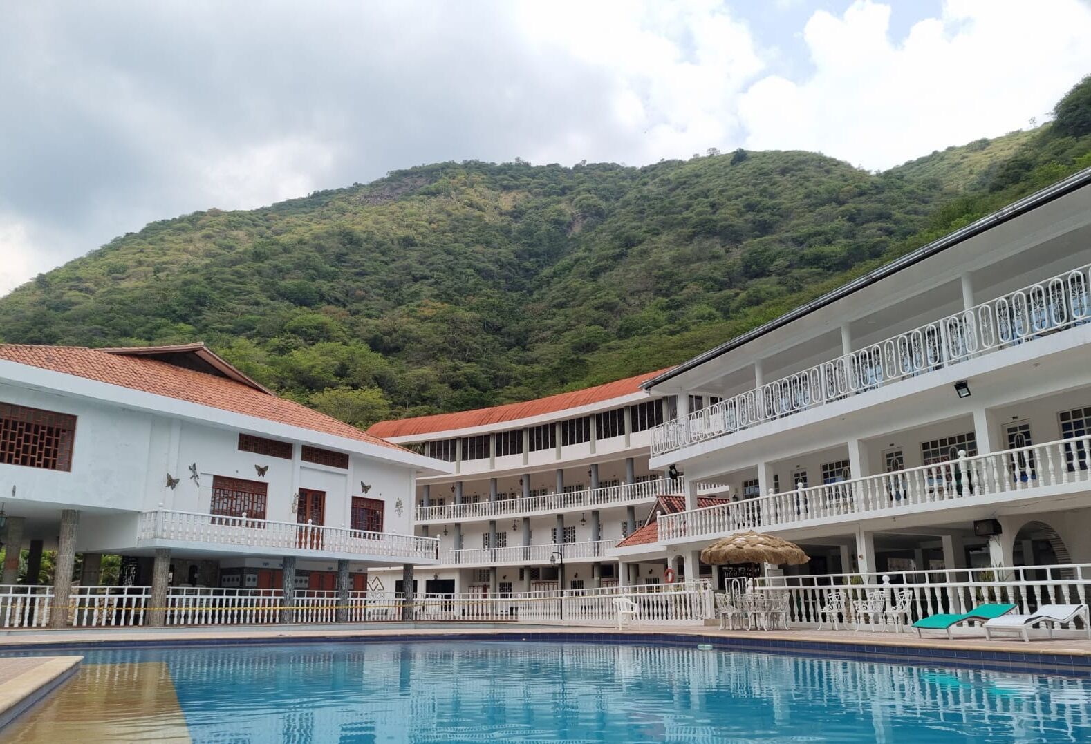 A hotel with a pool, multiple balconies, and a mountainous backdrop.