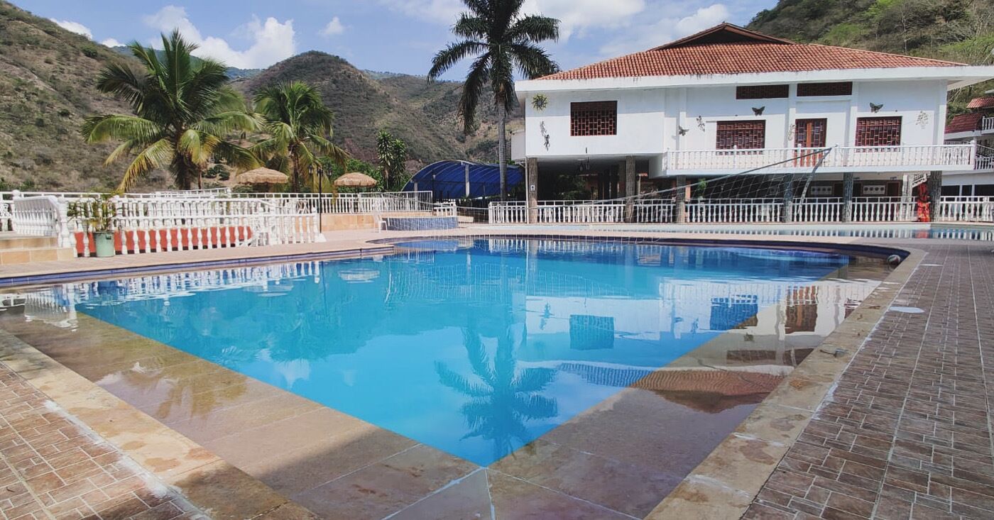 Una piscina con valla blanca, palmeras y un edificio con techo de tejas rojas.