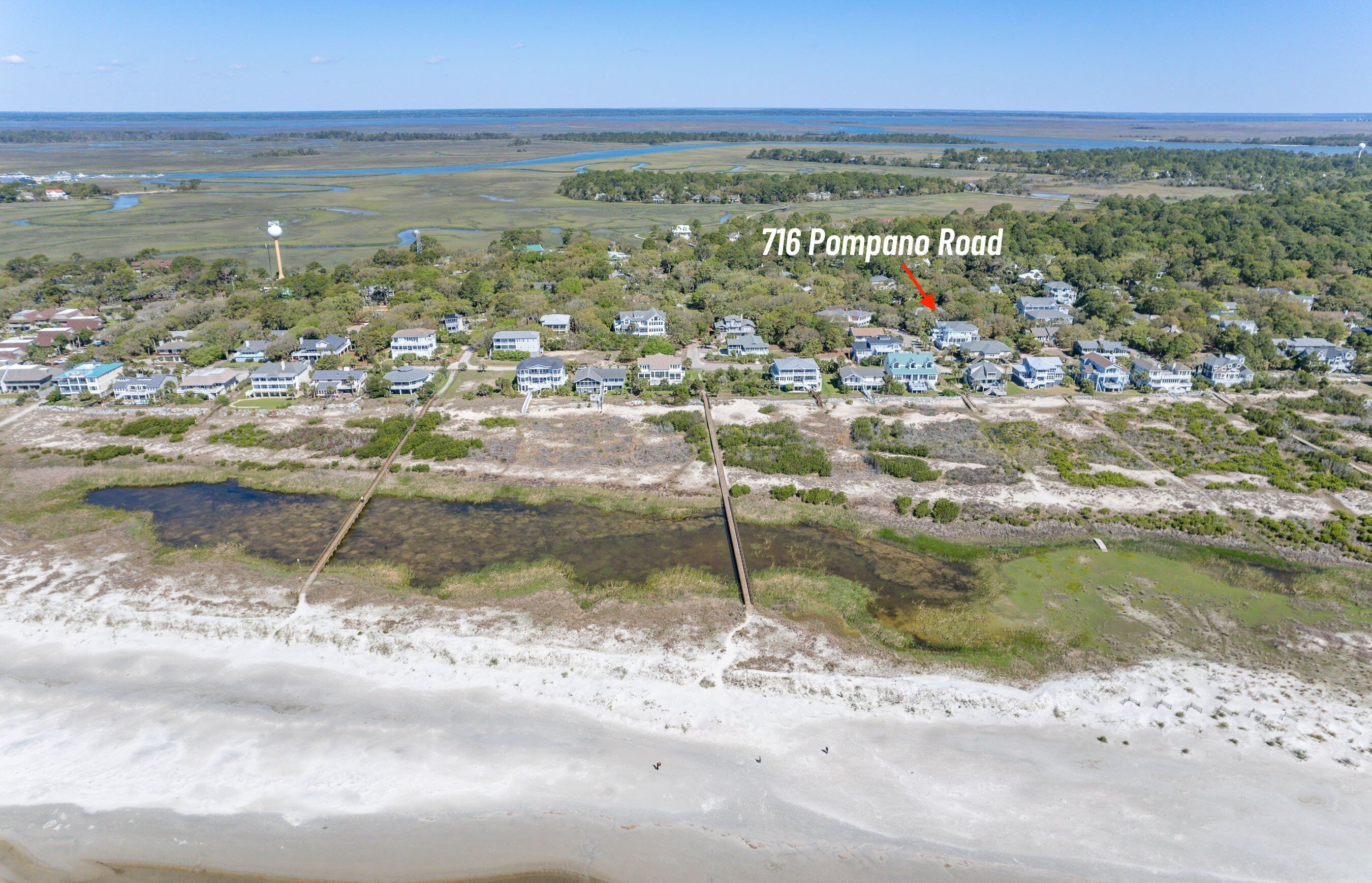 Vue aérienne d’un quartier résidentiel avec des maisons, une route portant l’inscription « 716 Pompano Road » et un plan d’eau au premier plan.