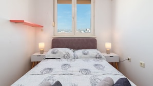 A bedroom with a bed, two bedside tables, a window, and a red shelf.
