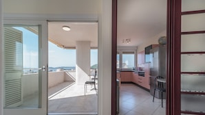 A modern kitchen with a view to the balcony, a dining area with chairs, and a large window.
