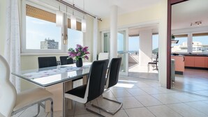 A modern dining area with a glass table, black chairs, and a vase of purple flowers.