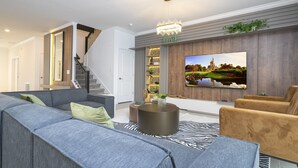 A modern living room with a grey sofa, a round coffee table, and a TV mounted on the wall. - The Ultimate 9bd Disney Getaway - The Best Arcade - Private Pool  (Kissimmee)