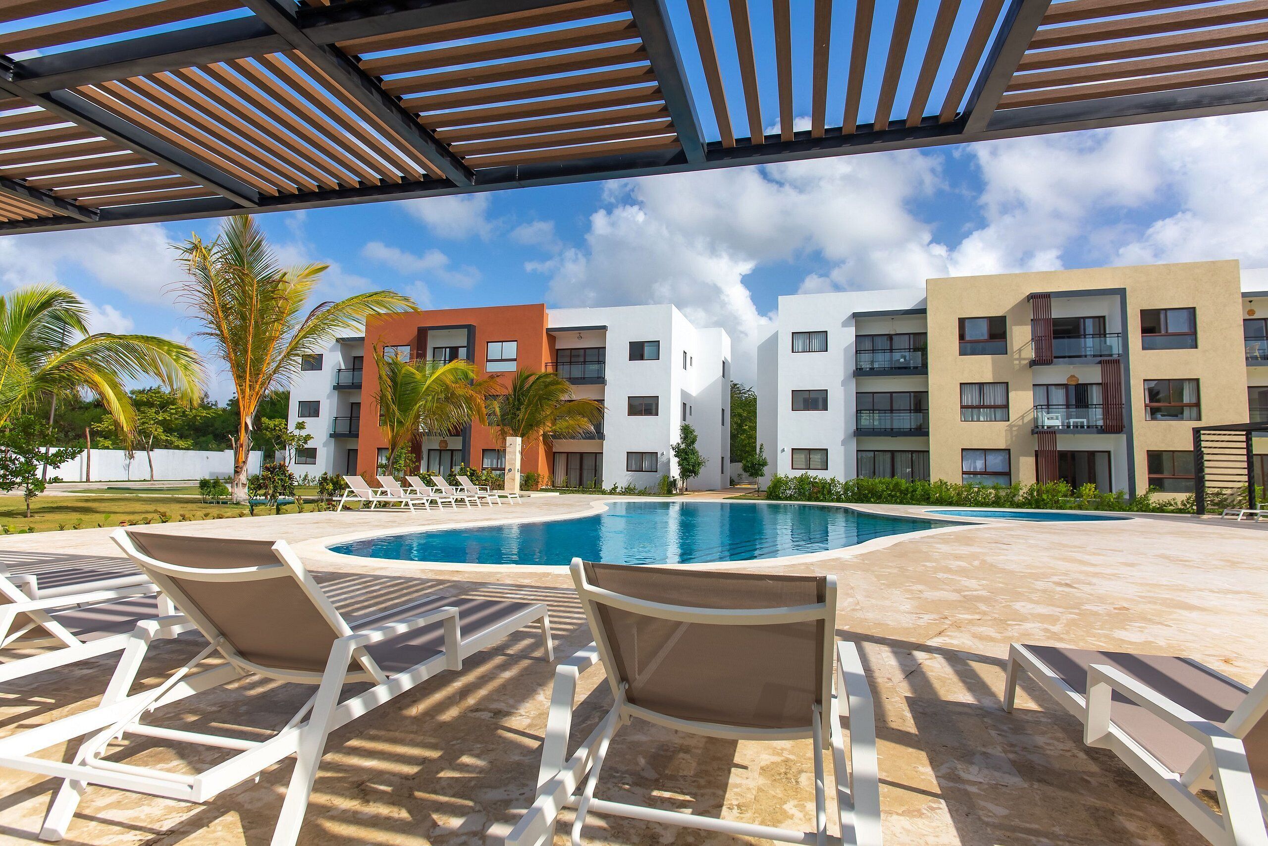 A pool area with lounge chairs, a clear sky, and modern buildings in the background.