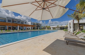 A swimming pool with lounge chairs and umbrellas, surrounded by modern buildings and palm trees.