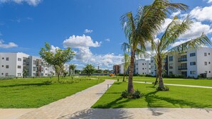 A modern residential complex with a central pathway, surrounded by greenery and palm trees. - Near the beach with pool and gym (Punta Cana)