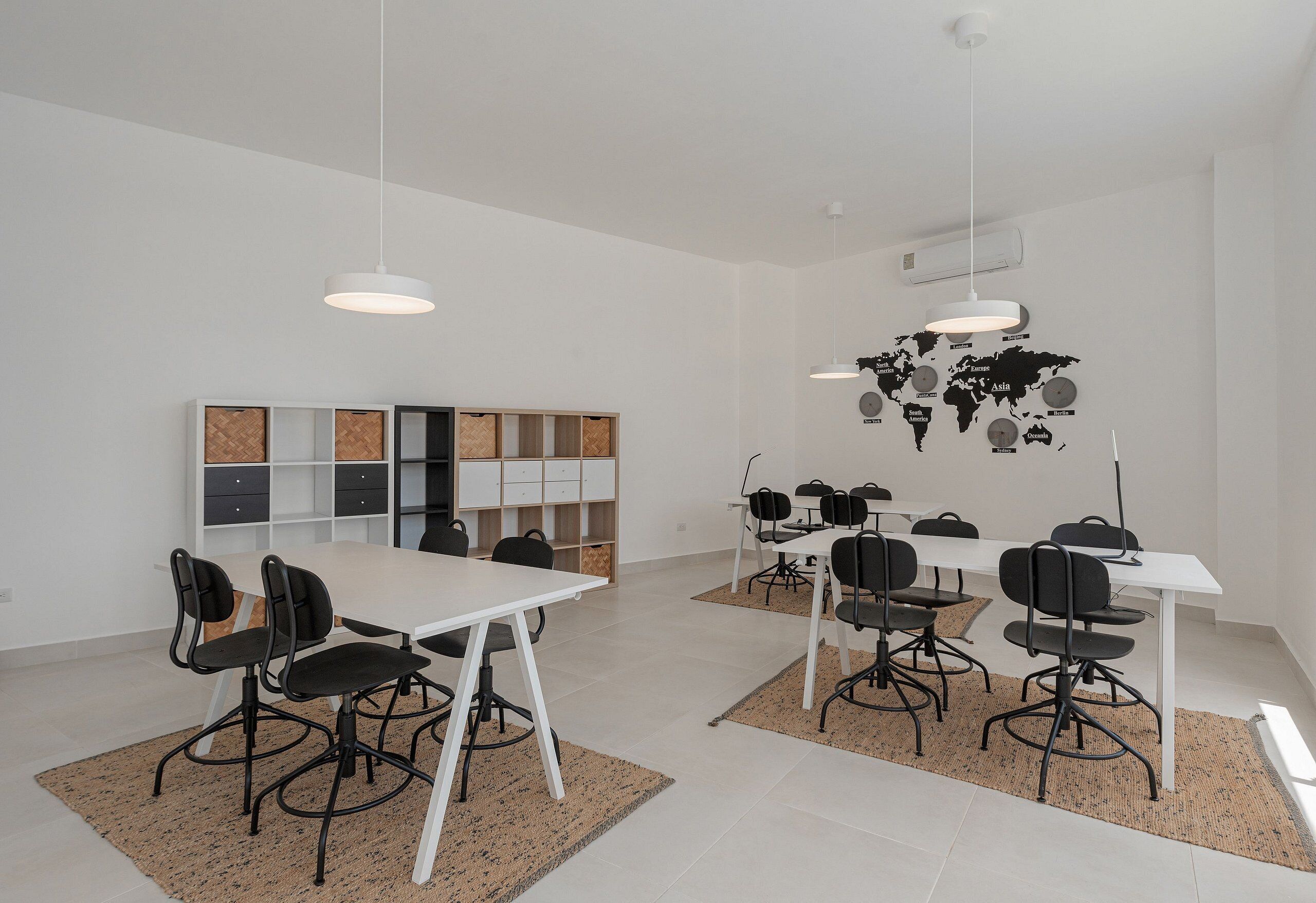 A modern meeting room with white tables and black chairs, a world map on the wall, and a bookshelf with cork boards.