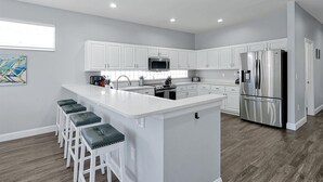 A modern kitchen with white cabinetry, a stainless steel refrigerator, a microwave, and a large island with bar stools. - Rest & Relax at Sunset by the Lake.  Entire Villa with Heated Pool and Spa! (Kissimmee)