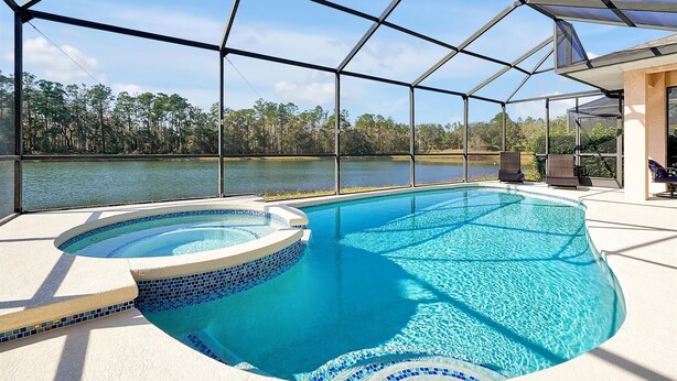 A swimming pool with a view of a lake and trees, surrounded by a covered area with chairs. - Rest & Relax at Sunset by the Lake.  Entire Villa with Heated Pool and Spa! (Kissimmee)