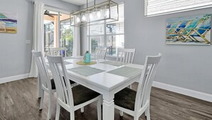 A dining area with a white table and chairs, a hanging light fixture, and artwork on the walls. - Rest & Relax at Sunset by the Lake.  Entire Villa with Heated Pool and Spa! (Kissimmee)
