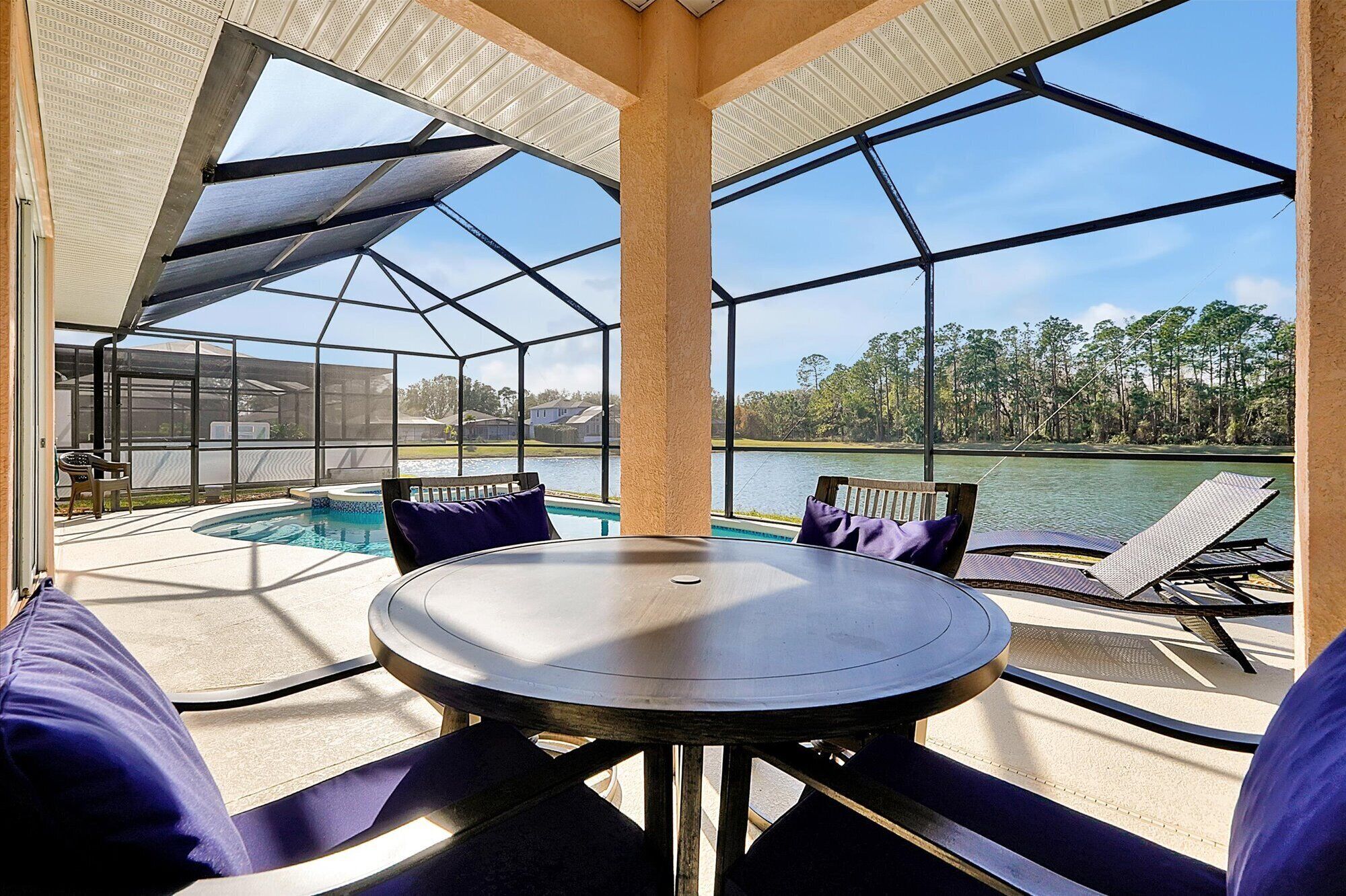 A covered outdoor area with a pool, lounge chairs, and a table.
