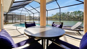 A covered outdoor area with a pool, lounge chairs, and a table. - Rest & Relax at Sunset by the Lake.  Entire Villa with Heated Pool and Spa! (Kissimmee)