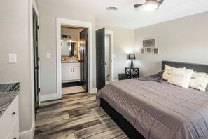 A bedroom with a bed, a nightstand, a lamp, a door leading to a bathroom, and a ceiling fan. - Riverfront Condo, Super Conveniently Located! (Townsend)