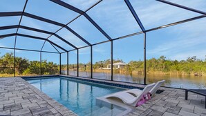 An indoor swimming pool with a clear view of the surrounding landscape, a covered patio area, and a herringbone-patterned floor. - Brandnew (2024) Villa with huge pool on the water (Port Charlotte)