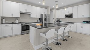 A modern kitchen with white cabinets, stainless steel appliances, a central island with bar stools, and pendant lighting. - Brandnew (2024) Villa with huge pool on the water (Port Charlotte)