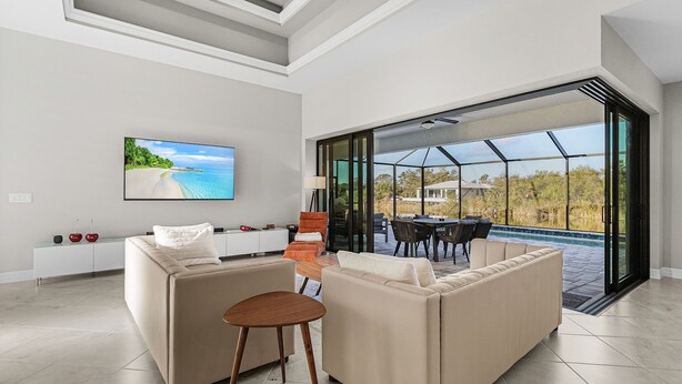 A modern living room with a large TV, comfortable seating, and a glass door leading to an outdoor area. - Brandnew (2024) Villa with huge pool on the water (Port Charlotte)