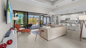 A modern living room with a sofa, a coffee table, and a TV on a stand. There is a kitchen area with a dining table and chairs. - Brandnew (2024) Villa with huge pool on the water (Port Charlotte)