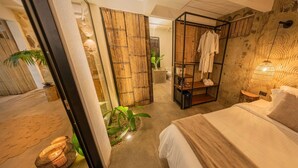 Un dormitorio moderno con cama, un armario de madera, un escritorio pequeño y un baño visible a través de una puerta abierta.