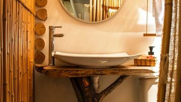 Un bagno con parete in bambù, uno specchio rotondo, un lavabo fissato a un ceppo d'albero e un water.