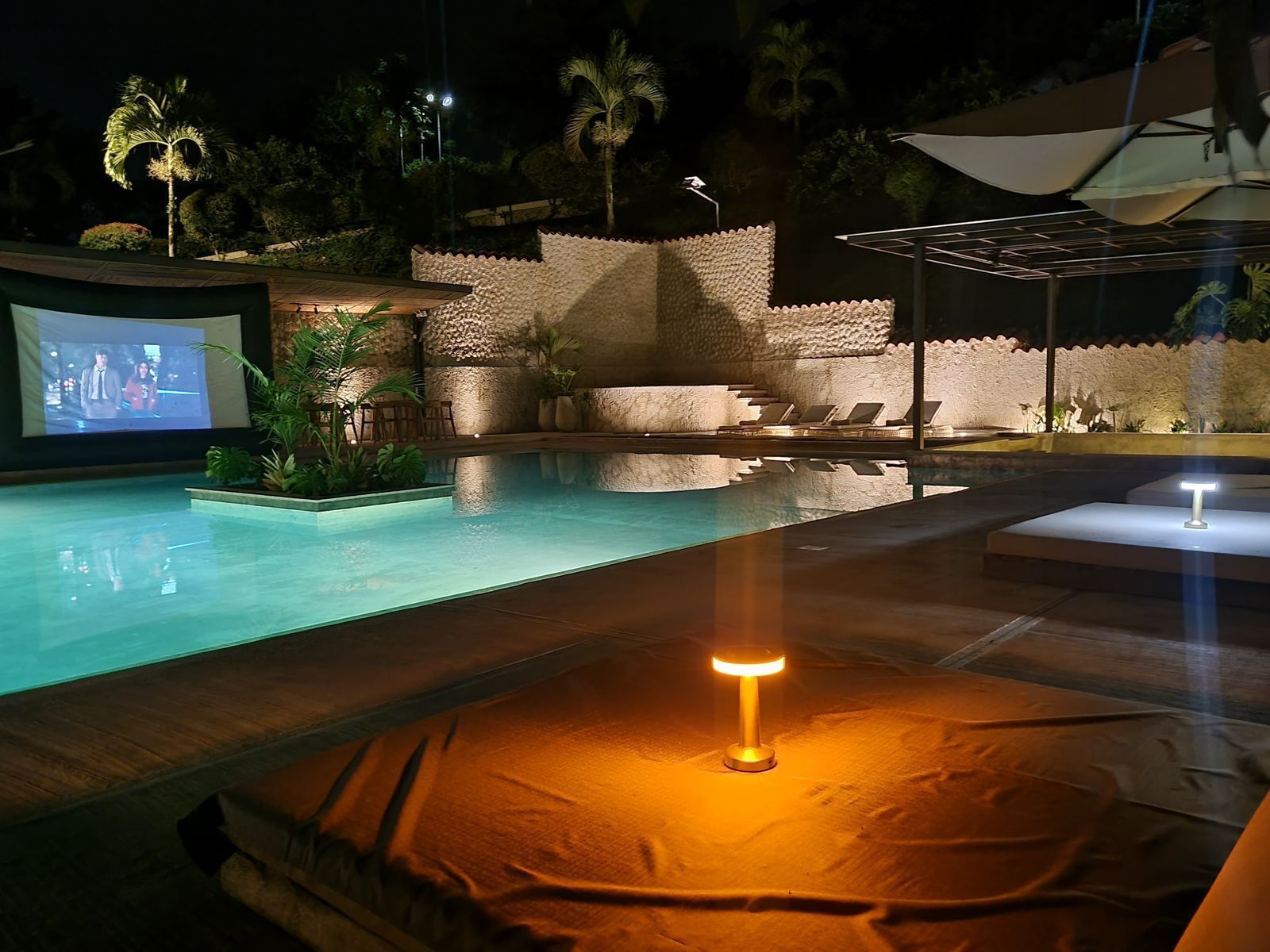 Una piscina con pared de piedra y pantalla de proyección.