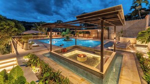 Un área de piscina con un hoyo de fuego, sillones de descanso y una pérgola.
