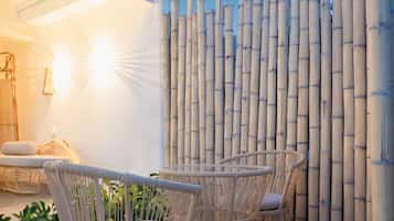 A bamboo fence, wicker chairs, and a white wall with a window.