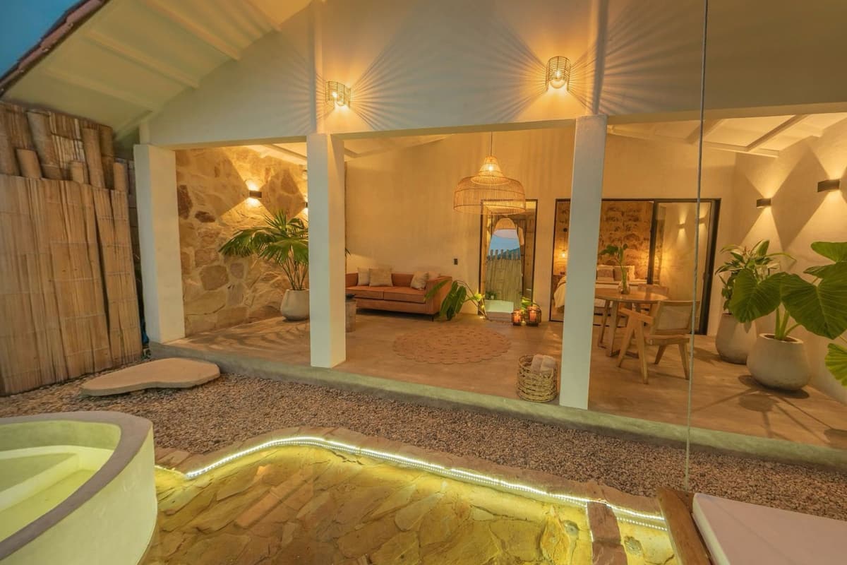 Un espacio exterior moderno con pared de piedra, zona de estar con cojines y comedor.