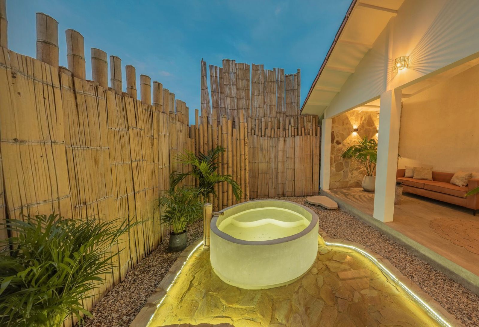Zona de spa con bañera de hidromasaje, valla de bambú y pared de piedra.