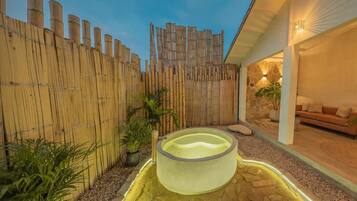 Zona de spa con bañera de hidromasaje, valla de bambú y pared de piedra.