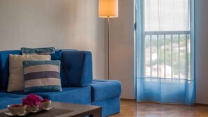 A living room with a blue sofa, a floor lamp, and a view through sheer curtains. - Holiday apartment with partial sea view (Vrbnik)