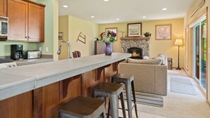 Una cocina con armarios de madera, chimenea de piedra y una zona de bar con taburetes.