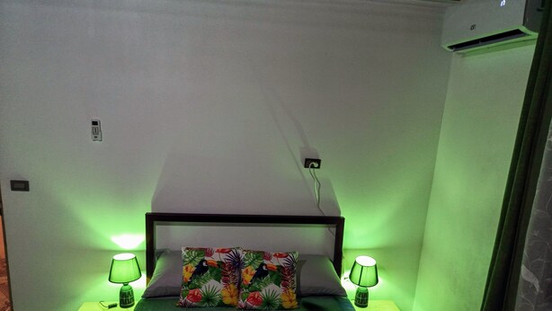 Un dormitorio pequeño y acogedor con una cama individual, iluminación ambiental verde y una almohada con temática tropical.