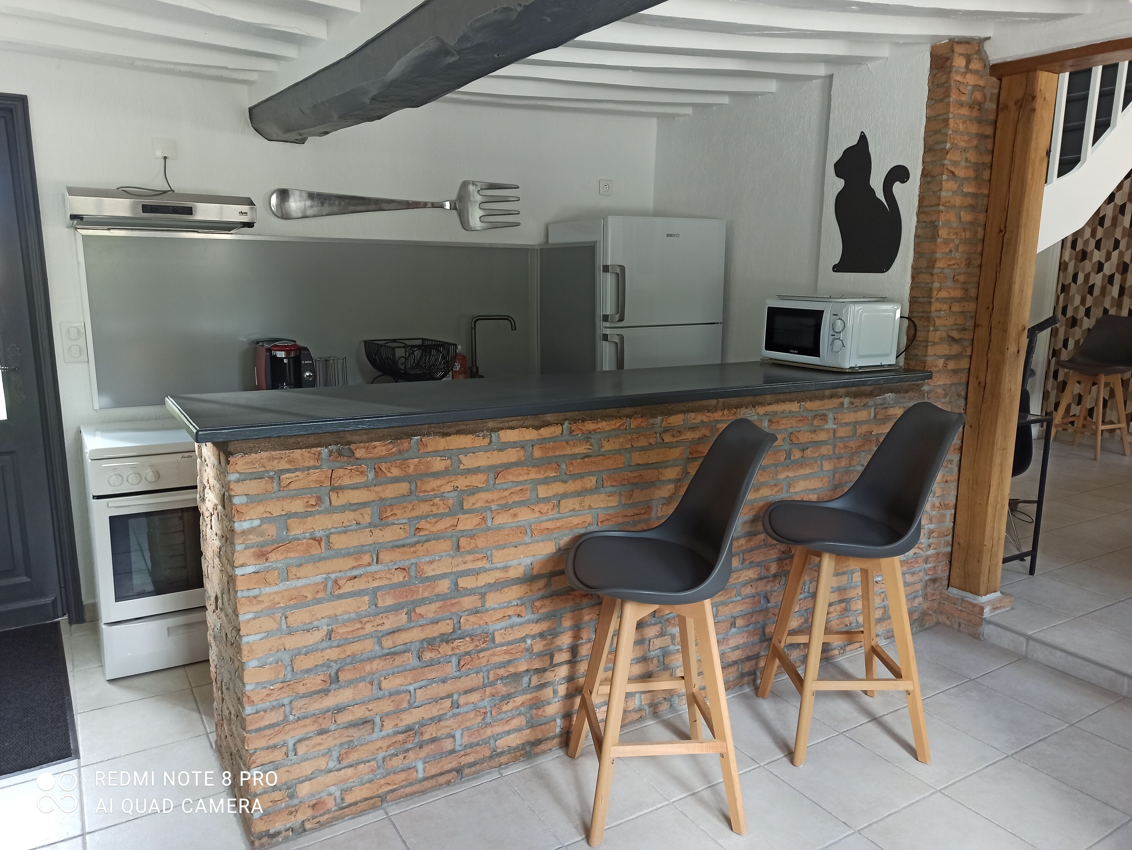 A kitchen with a brick wall, a microwave, a refrigerator, and two bar stools.