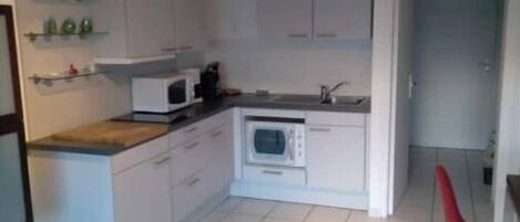 A modern kitchen with white cabinets, a microwave, and a sink. There is a red chair and a small dining table.
