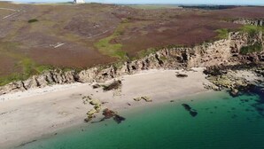 A coastal landscape with a beach, cliffs, and a distant building. - House of the Northern Gate (Thurso)