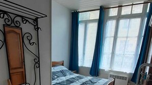 Een slaapkamer met een houten bed, een radiator, een raam met gordijnen en een metalen rek.
