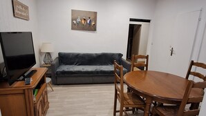 Een woonkamer met een televisie, bank, eettafel en stoelen.