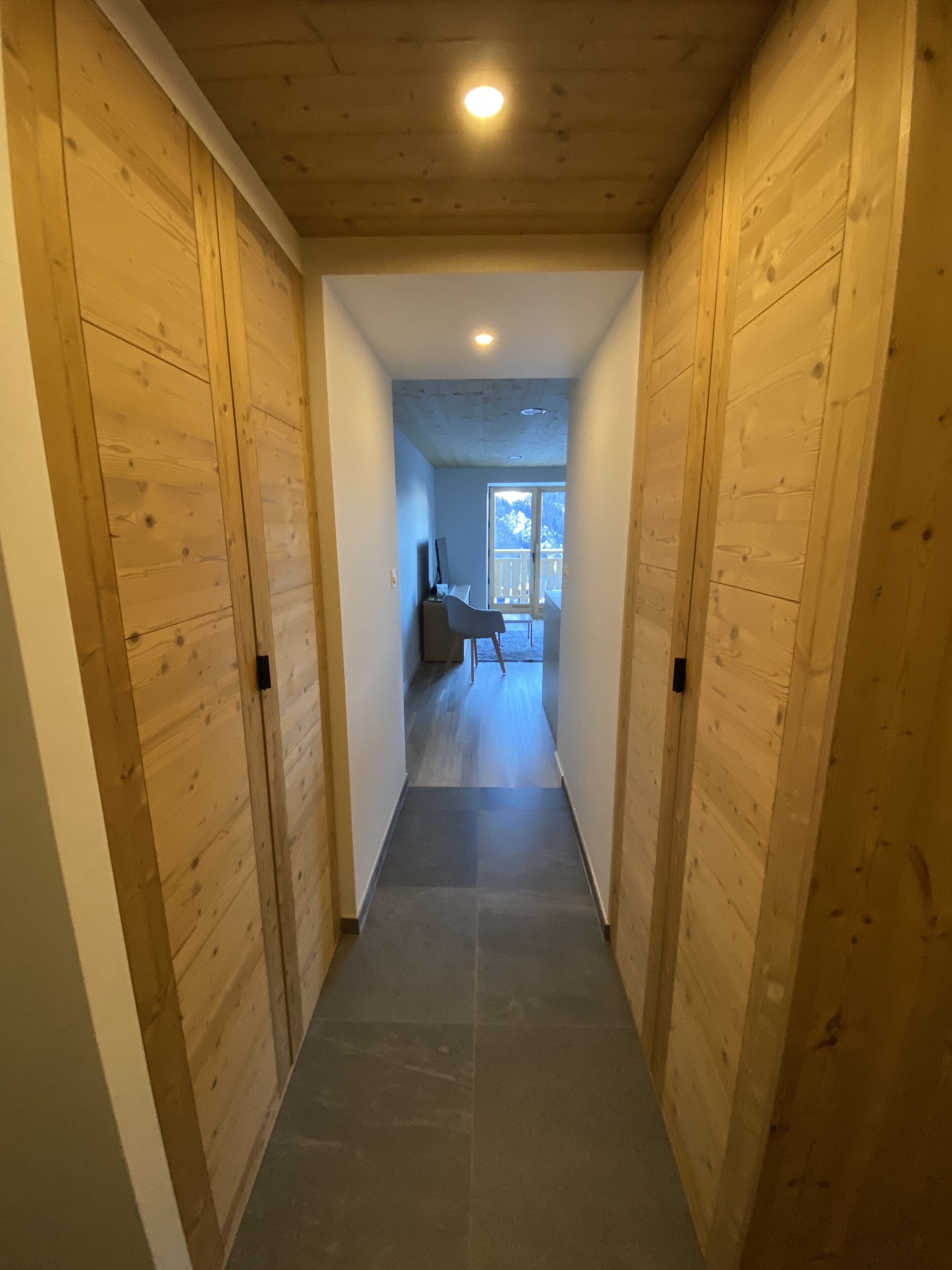 Ein Korridor mit Holzwänden und Fliesenboden, der zu einem Raum mit Fenster und Stuhl führt.