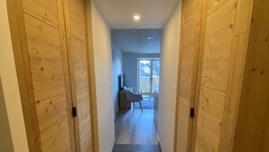 A hallway with wooden walls and a tiled floor, leading to a room with a window and a chair.