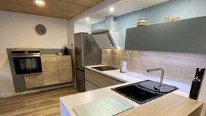 A modern kitchen with wooden cabinets, a built-in oven, a stainless steel refrigerator, a sink, and a countertop.