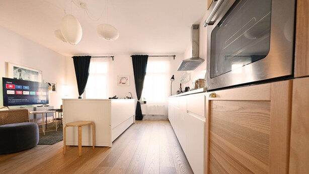 A modern kitchen with wooden cabinets, a built-in oven, and a dining area with a small table and chairs. - Enchanting Suite in the Heart of Brussels (Bruxelles)