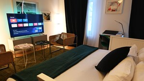 A hotel room with a bed, a TV displaying a home screen, a chair, a small table, and a lamp. - Enchanting Suite in the Heart of Brussels (Bruxelles)