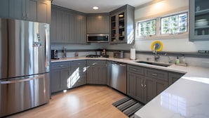 A modern kitchen with grey cabinets, stainless steel appliances, and a large window providing natural light. - Serene Lakefront Home On Lake Minnetonka (Excelsior)