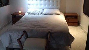 Ein Schlafzimmer mit einem großen Bett, zwei Nachttischen, einem Sessel und einem kleinen Tisch.