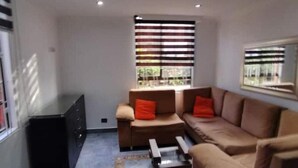 Ein Wohnzimmer mit einem braunen Sofa, einem kleinen Couchtisch und einem Fenster mit gestreiften Jalousien.