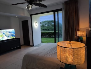 A modern bedroom with a television, a large bed, a ceiling fan, and a view of the outdoors.