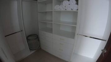 Habitación compacta con armario, un cesto de basura pequeño y estantes con toallas enrolladas.