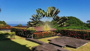Ein angelegter Garten mit einer Palme, Blumenbeeten und Blick auf den Ozean.