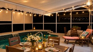 Ein Essbereich im Freien mit Pool, Lichterketten und einer überdachten Lounge-Ecke.