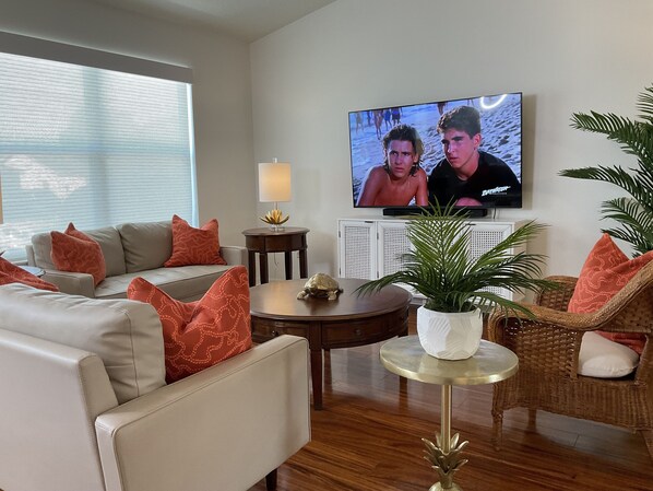 Ein Wohnzimmer mit einer Couch, Sesseln, einem Couchtisch, einem Fernseher und einer Zimmerpflanze.
